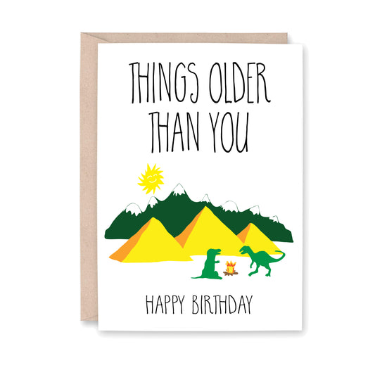 Greeting card with a smiling sun, snow capped mountains, egyptian pyramids, two dinosaurs and a fire, that reads "Things older than you. Happy Birthday!"